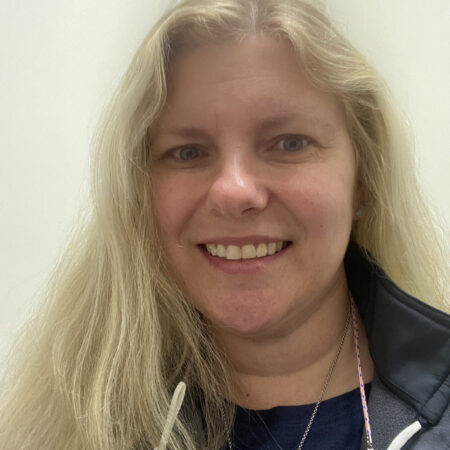 Headshot of Julie M. Meyer. She has medium length blonde hair and is wearing a blue and green jacket, smiling.