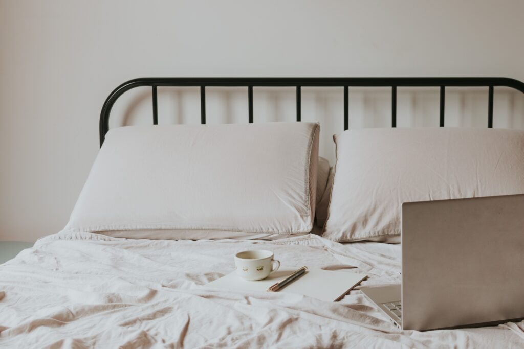 Minimalist home office setup with laptop on bed, coffee cup, and notes for a comfortable work environment.