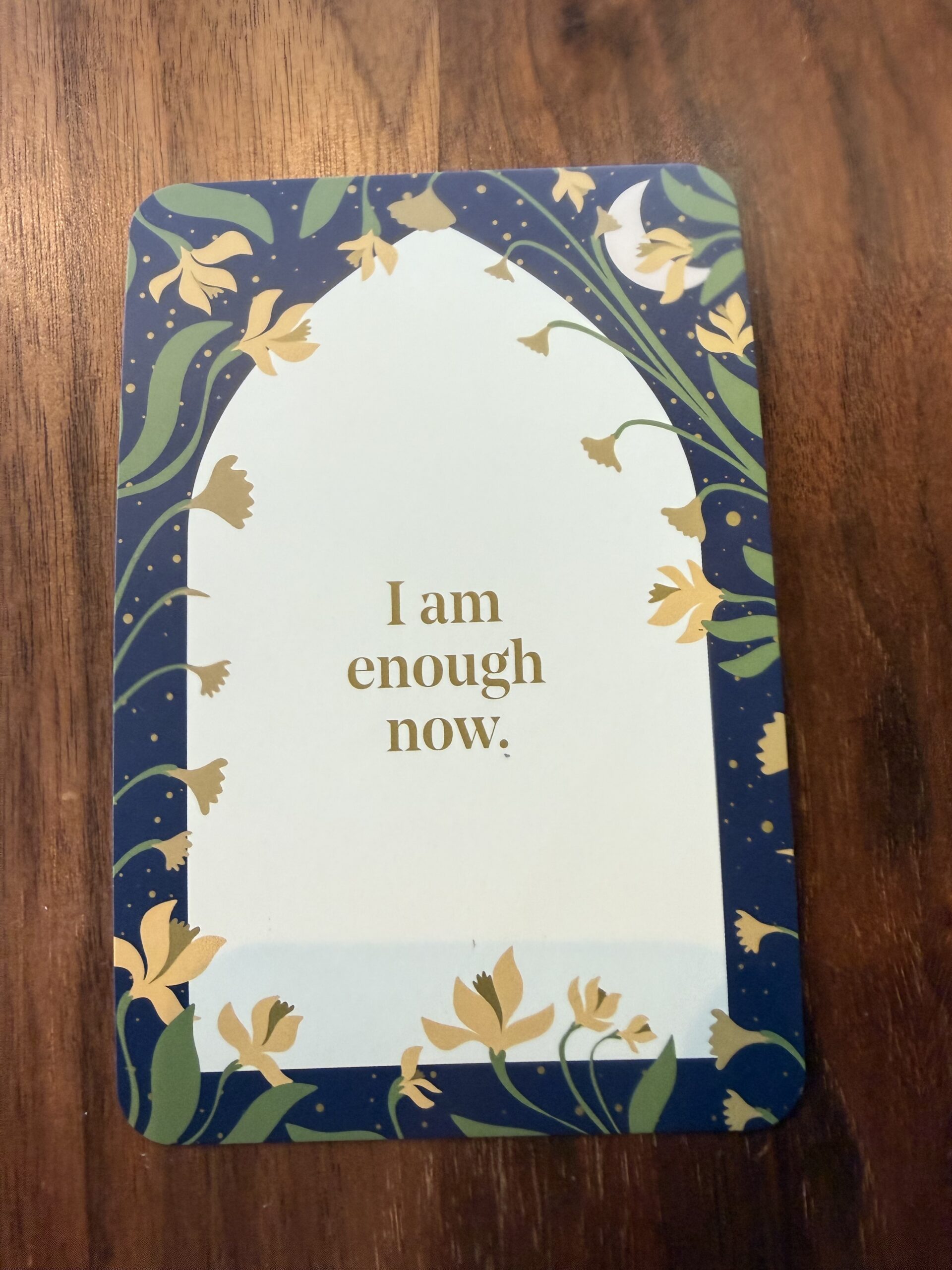 Card that says "I am enough now", sitting on a wooden table.